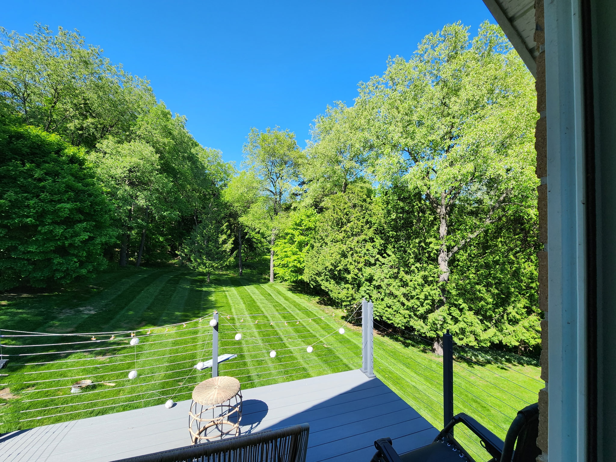 Striped backyard lawn viewed from a deck framed by mature trees