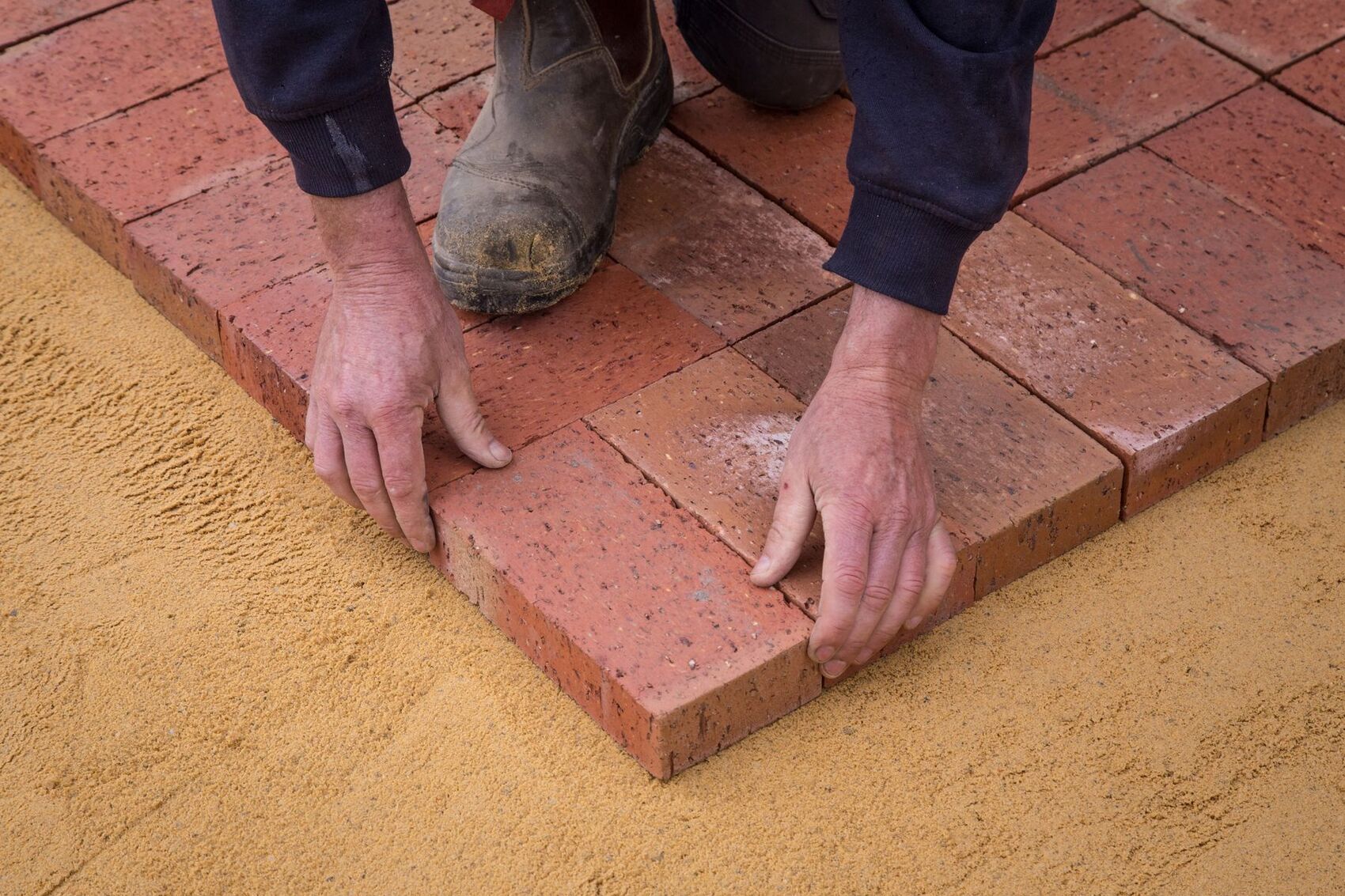 Installer setting clay pavers into a screeded sand base during a patio build