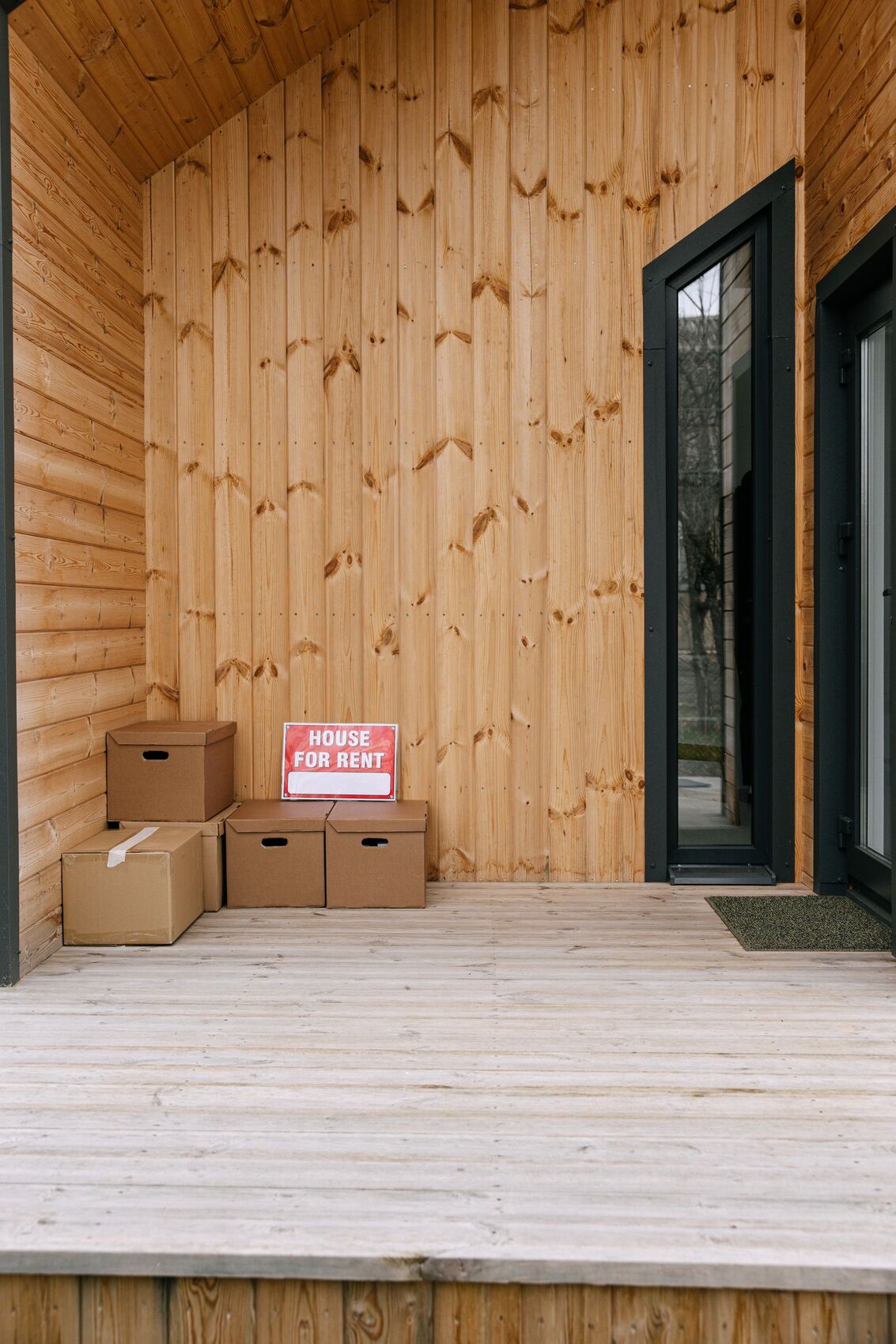 Moving boxes and a house-for-rent sign on the porch of a vacant rental property